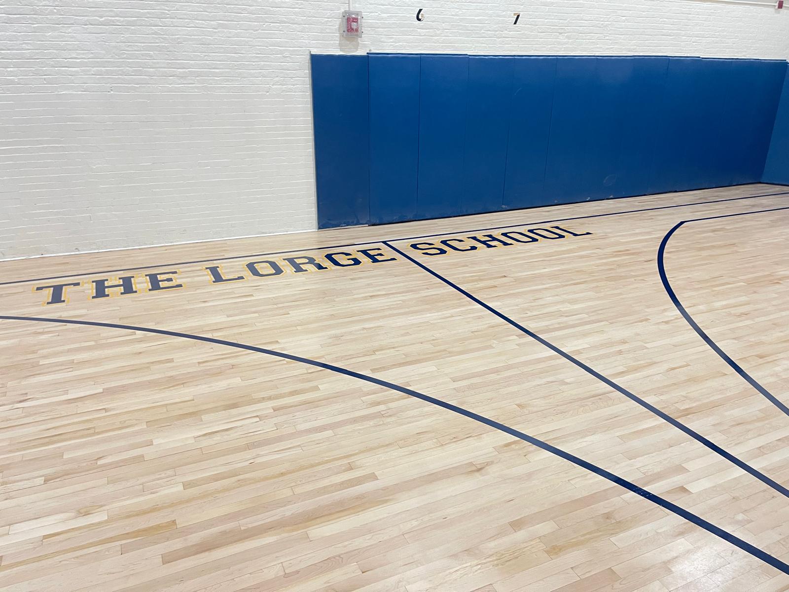 Restored basketball court at The Lorge School with fresh maple, navy lines and gold-outlined lettering