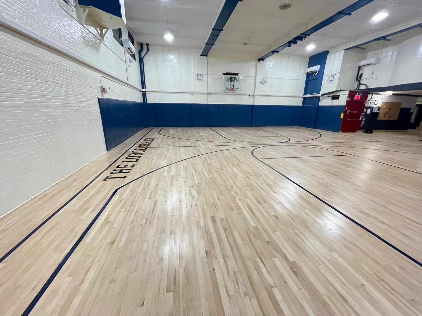 Same basketball court after restoration — bright maple with crisp navy lines and glossy finish