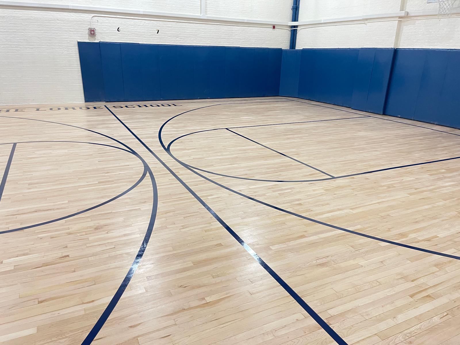 Wide view of the finished basketball court with navy lines on bright maple