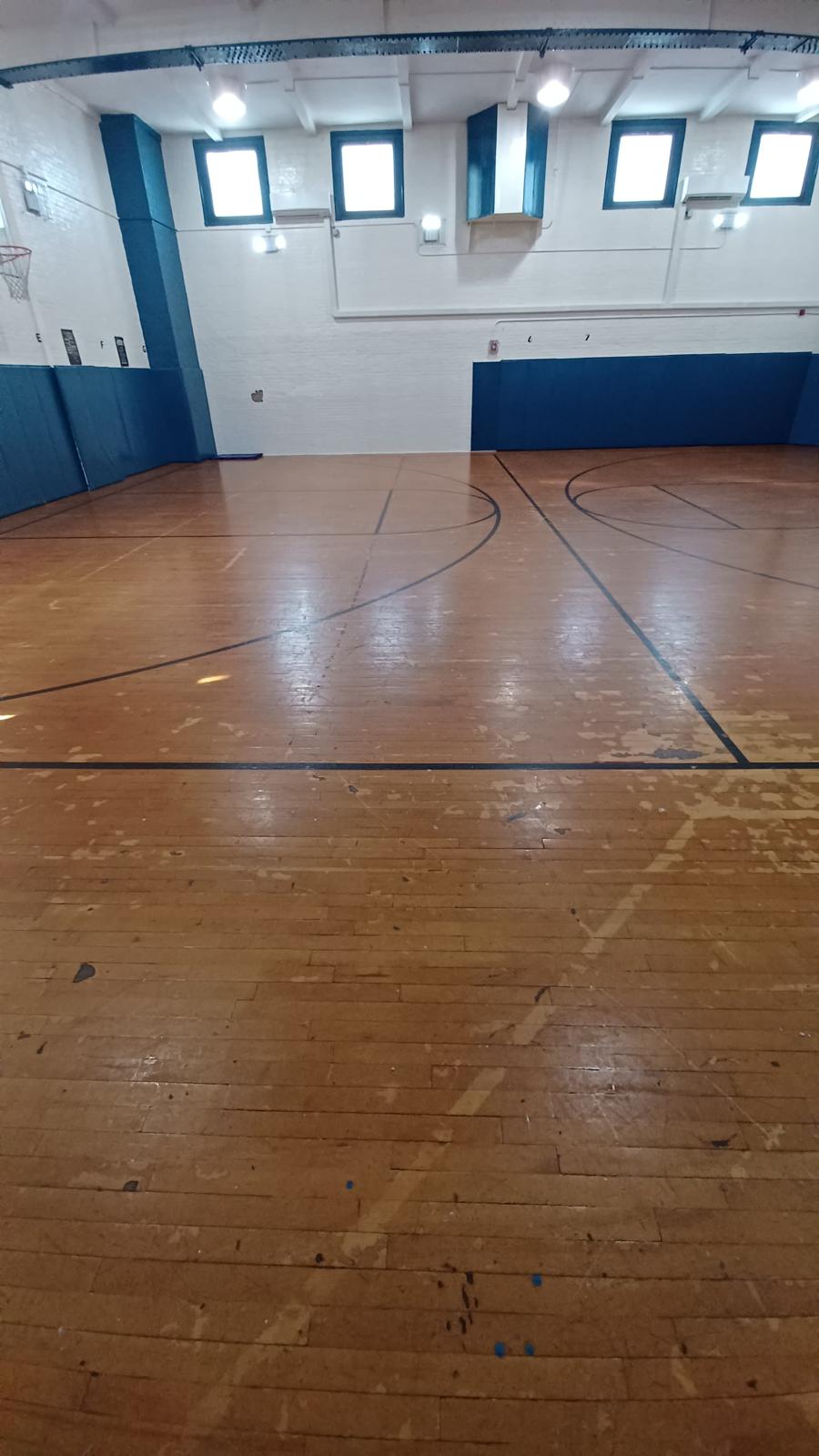 Basketball court before restoration — worn, scratched floor with faded lines