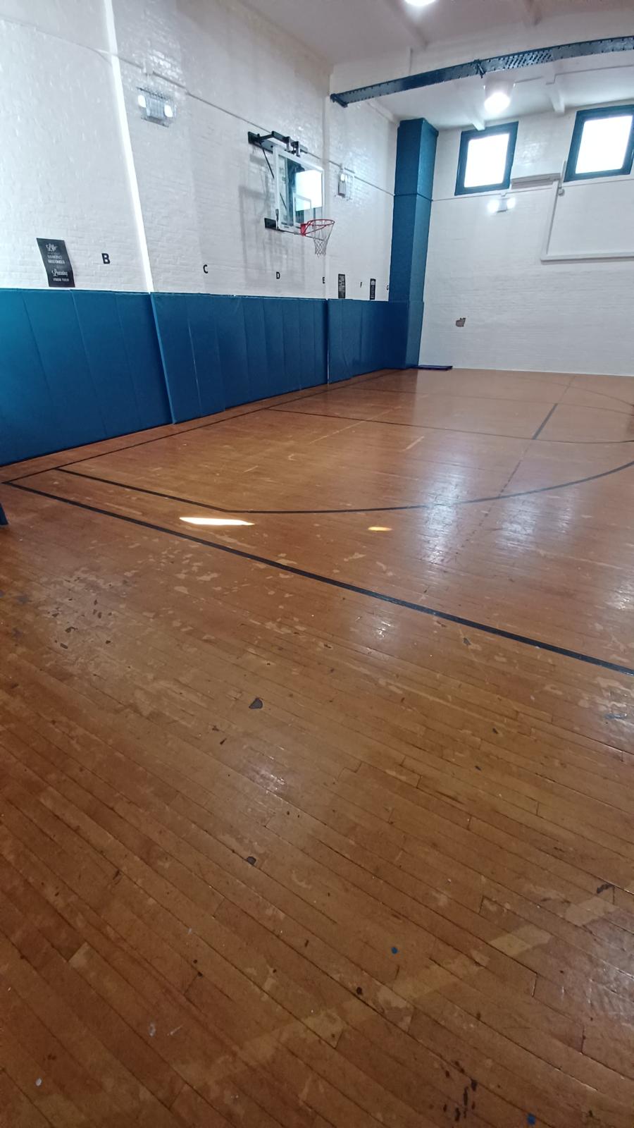 Basketball court before restoration — dark, stained boards and worn old lines